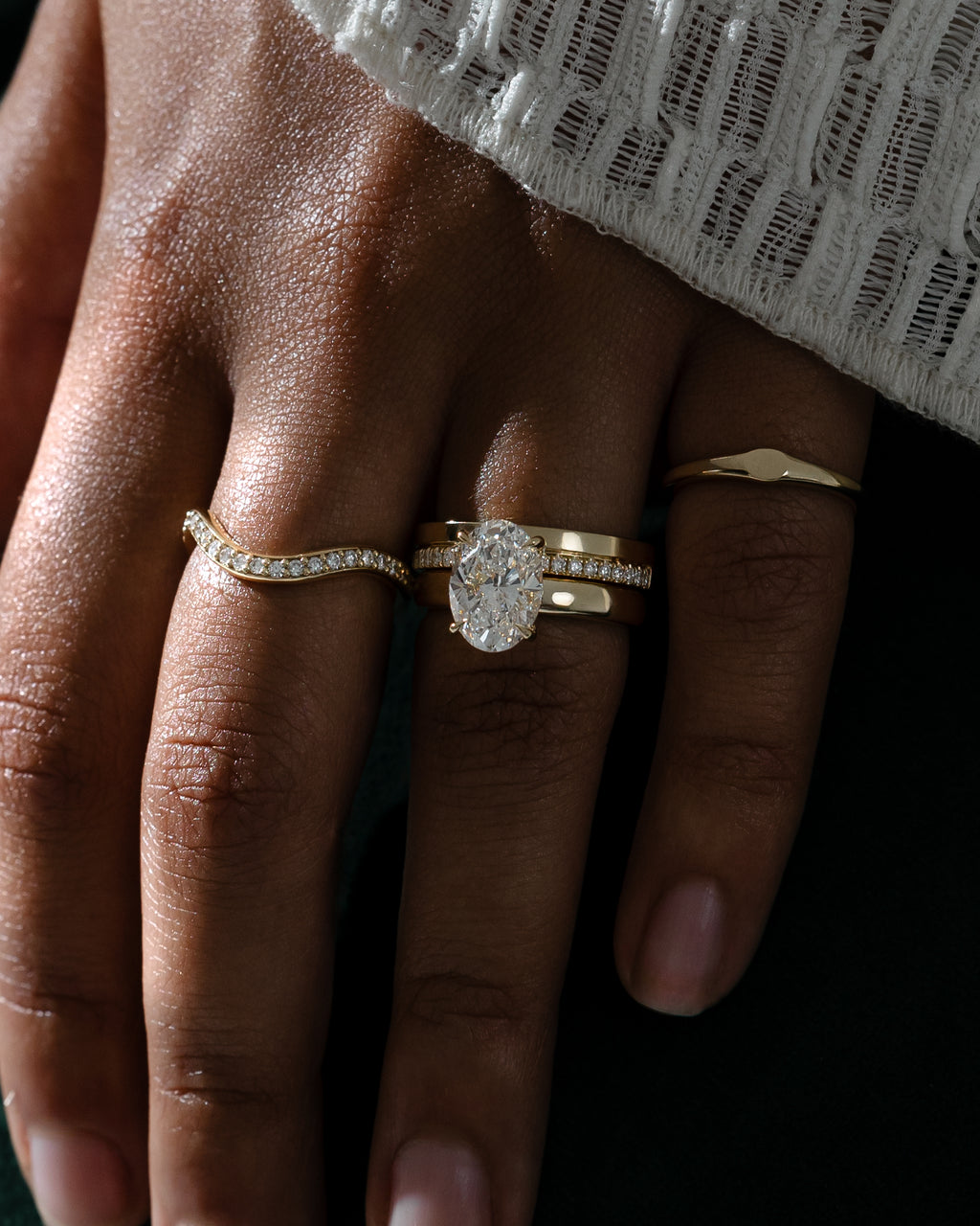 MET 0381 yellow-gold edge-pavé cigar band worn on the ring finger beneath a separate oval solitaire. Additional rings shown for styling are not included.